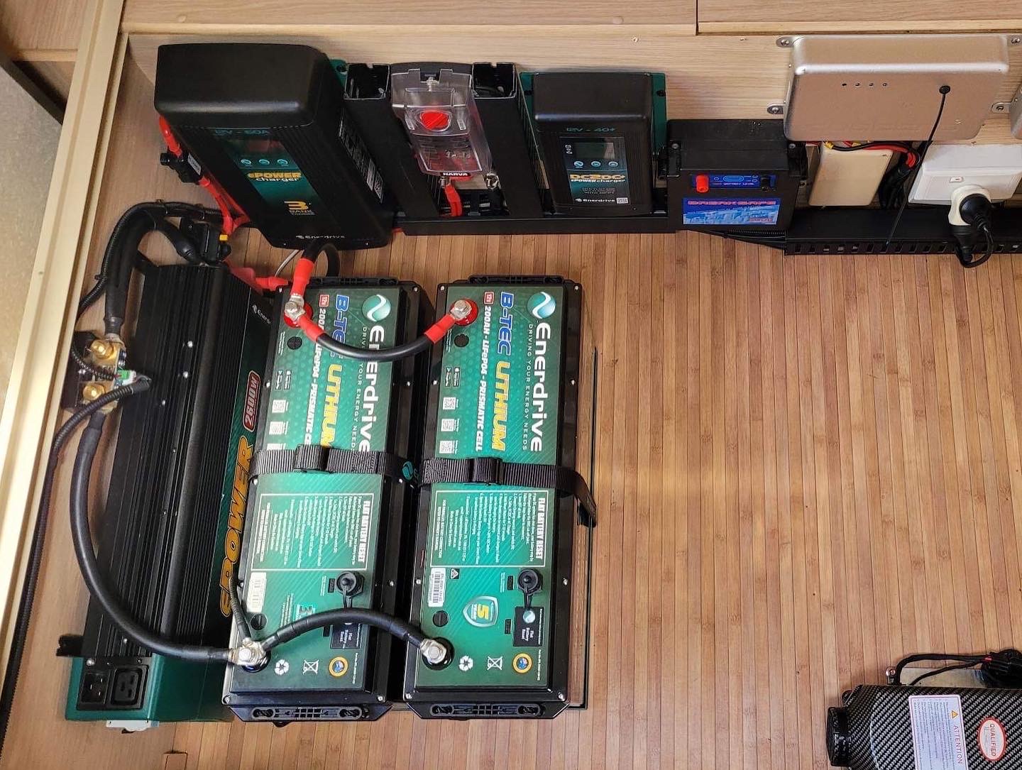 Twin lithium batteries, DC charger and busbars laid out on a timber floor